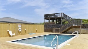 Una terraza de madera con una piscina rectangular, una silla blanca y una estructura de madera con escaleras.