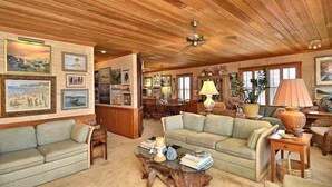 A cozy living room with wooden ceilings, a sofa, a coffee table, and framed pictures on the walls. - Gorgeous old nags head oceanfront home with spacious decks and beautiful views! (Nags Head)