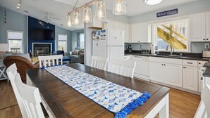 A modern kitchen with white cabinets, a wooden dining table, and a sign reading "BEACH HOUSE." - Updated semi-oceanfront home in quiet South Nags Head! (Nags Head)