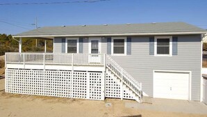 A two-story house with a covered porch, a fenced deck, and a garage. - South Nags Head cottage with hot tub! 3 minute walk to the beach. (Nags Head)