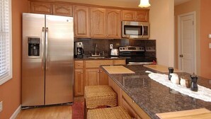 A modern kitchen with wooden cabinets, stainless steel appliances, and a granite countertop. - South Nags Head cottage with hot tub! 3 minute walk to the beach. (Nags Head)