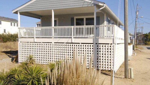 A two-story house with a balcony, a white fence, and a sandy ground. - South Nags Head cottage with hot tub! 3 minute walk to the beach. (Nags Head)