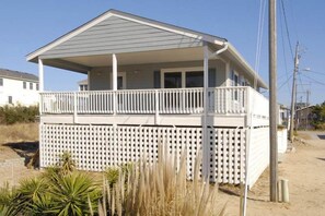 Une maison à deux étages avec un balcon, une clôture blanche et un sol sablonneux.
