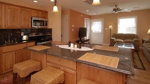 A modern kitchen with wooden cabinets, a central island, and a dining area with a sofa. - South Nags Head cottage with hot tub! 3 minute walk to the beach. (Nags Head)