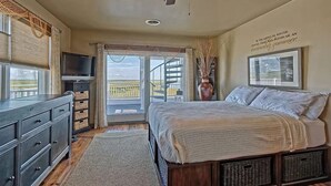 Un dormitorio con cama, ventilador de techo, televisor y ventana grande con vista a un balcón.