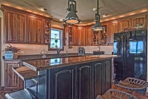 Una cocina con armarios de madera, encimera de granito, refrigerador negro e iluminación colgante.