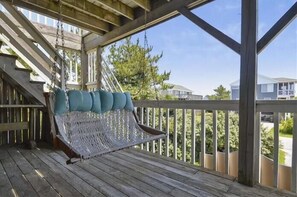 Terraza de madera con una hamaca colgante y baranda blanca.