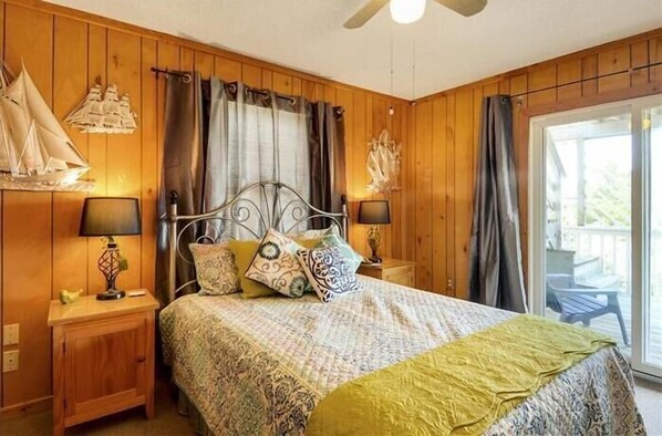 Un dormitorio con paneles de madera, una cama, dos mesitas de noche con lámparas y vistas al exterior a través de una puerta corredera de cristal.