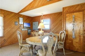 Uma sala de jantar com teto de madeira, mesa redonda e cadeiras decoradas.