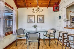 Un comedor con mesa de vidrio, cuatro sillas, una lámpara de araña y techo de madera.