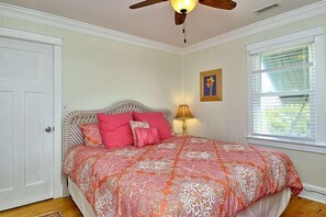 Un dormitorio con cama, ventilador de techo, ventana con persianas y una puerta.