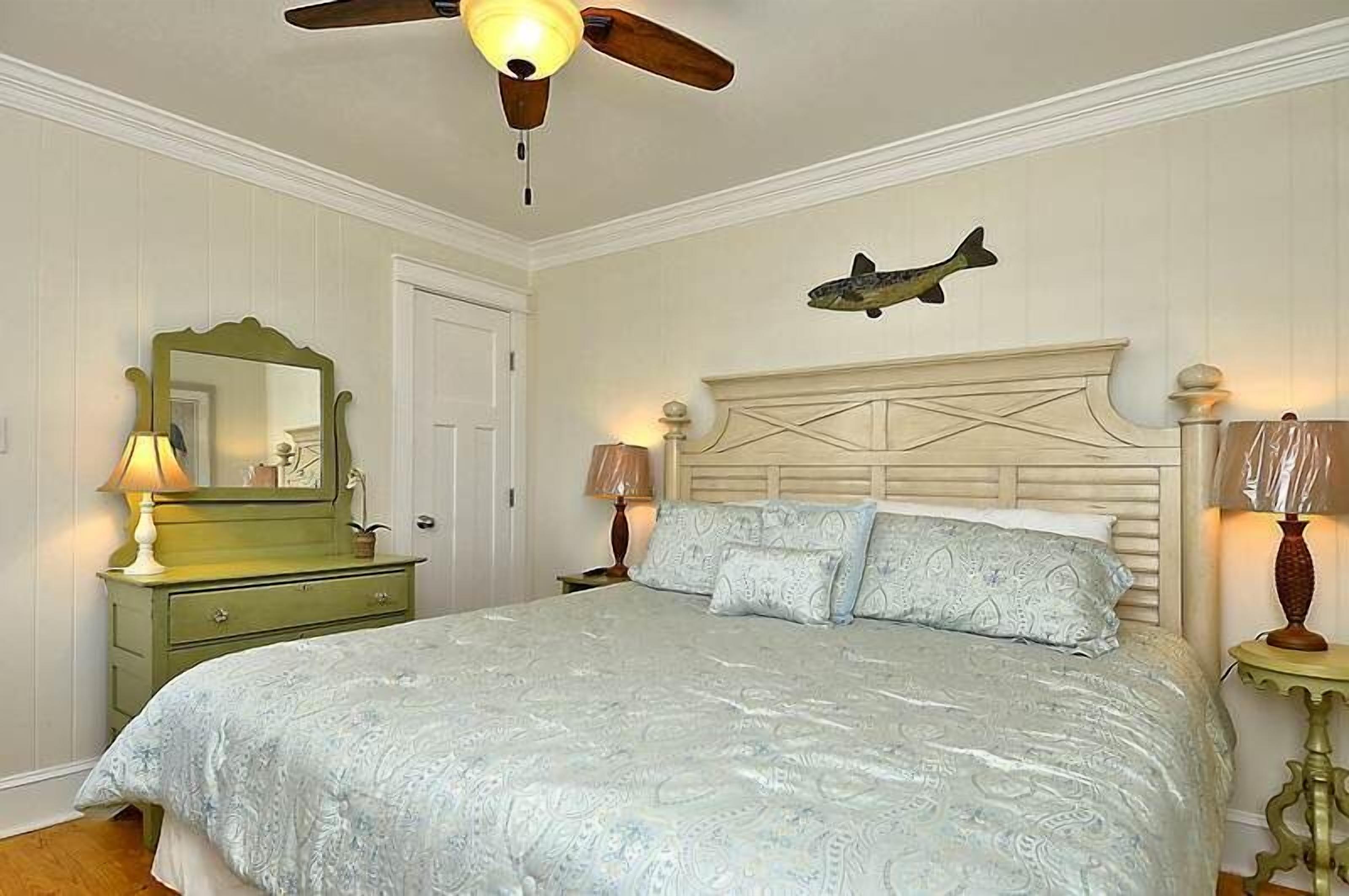 Une chambre à coucher comprenant un lit, une commode, un miroir, un ventilateur de plafond et un décor mural représentant des poissons.