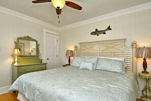 Une chambre à coucher comprenant un lit, une commode, un miroir, un ventilateur de plafond et un décor mural représentant des poissons.