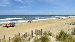 A beach with a wooden fence, a pier in the background, and people relaxing on the sand. - 5 bedroom, classic old nags head oceanfront home! (Nags Head)