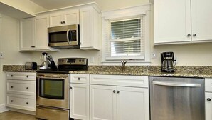 A kitchen with white cabinets, stainless steel appliances, a granite countertop, and a window with blinds. - 5 bedroom, classic old nags head oceanfront home! (Nags Head)