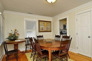 Une salle à manger avec une table et des chaises en bois, un vase de fleurs et un tableau au mur.