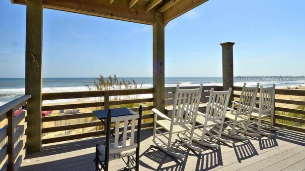 A wooden deck with white chairs overlooking a beach and ocean. - 5 bedroom, classic old nags head oceanfront home! (Nags Head)