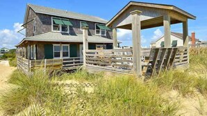 A wooden house with a porch and a covered area, surrounded by sand and grass. - 5 bedroom, classic old nags head oceanfront home! (Nags Head)