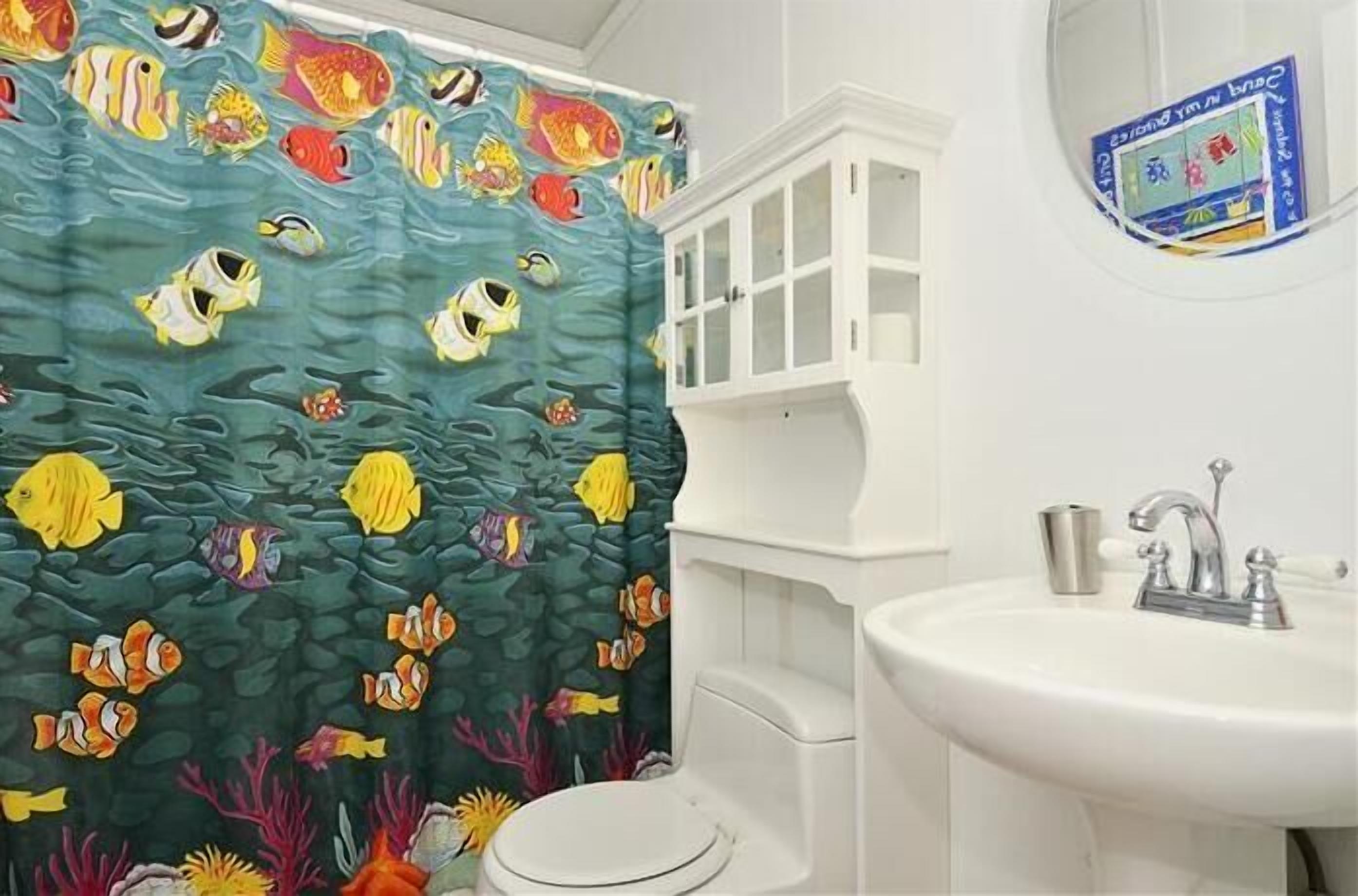 A bathroom with a shower curtain depicting underwater fish, a white sink, and a cabinet.