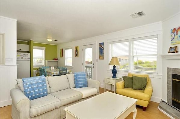 A living room with a beige sofa, a yellow sofa, and a white coffee table. There is a fireplace and a window with blinds.