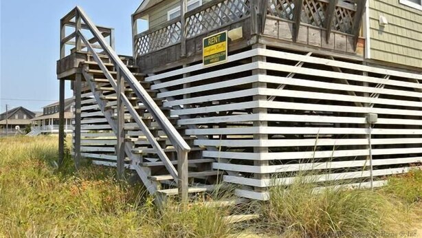 Eine Holzhütte mit einem 'RENT'-Schild, einer Treppe und einem eingezäunten Bereich.