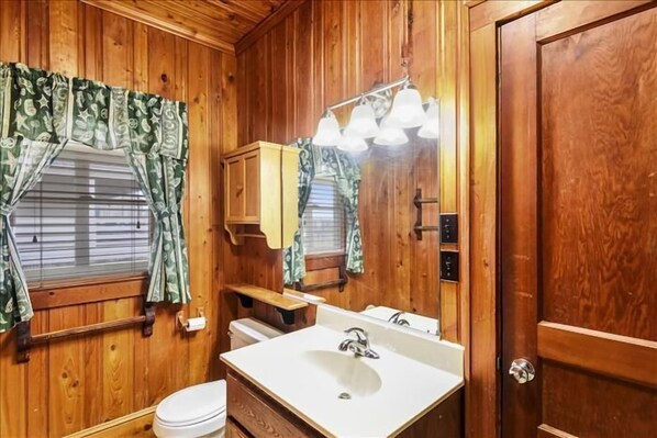 A wooden-paneled bathroom with a white sink, a mirror, and a window with patterned curtains. - Beautiful and classic OBX oceanfront home in KDH! Steps from the Avalon Pier. (Kill Devil Hills)