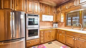 A kitchen with wooden cabinets, stainless steel appliances, and a window with blinds. - Beautiful and classic OBX oceanfront home in KDH! Steps from the Avalon Pier. (Kill Devil Hills)