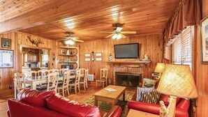 A wooden interior with a dining area, red leather sofa, television, fireplace, and ceiling fans. - Beautiful and classic OBX oceanfront home in KDH! Steps from the Avalon Pier. (Kill Devil Hills)