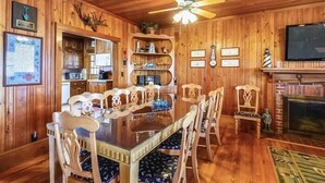 A wooden interior with a dining table, chairs, a ceiling fan, a fireplace, and a television. - Beautiful and classic OBX oceanfront home in KDH! Steps from the Avalon Pier. (Kill Devil Hills)