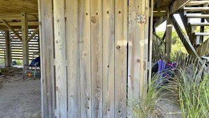 Eine Holzhütte mit schlichtem, rustikalem Design, inklusive Holzzaun und überdachter Fläche mit Erde als Boden.