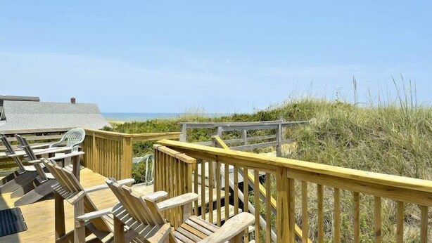Eine Holzterrasse mit Stühlen und Geländer mit Blick auf einen Strand.