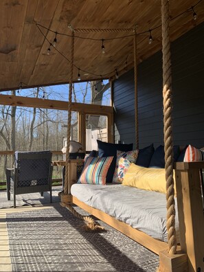 A wooden deck with a bed, pillows, and a chair.