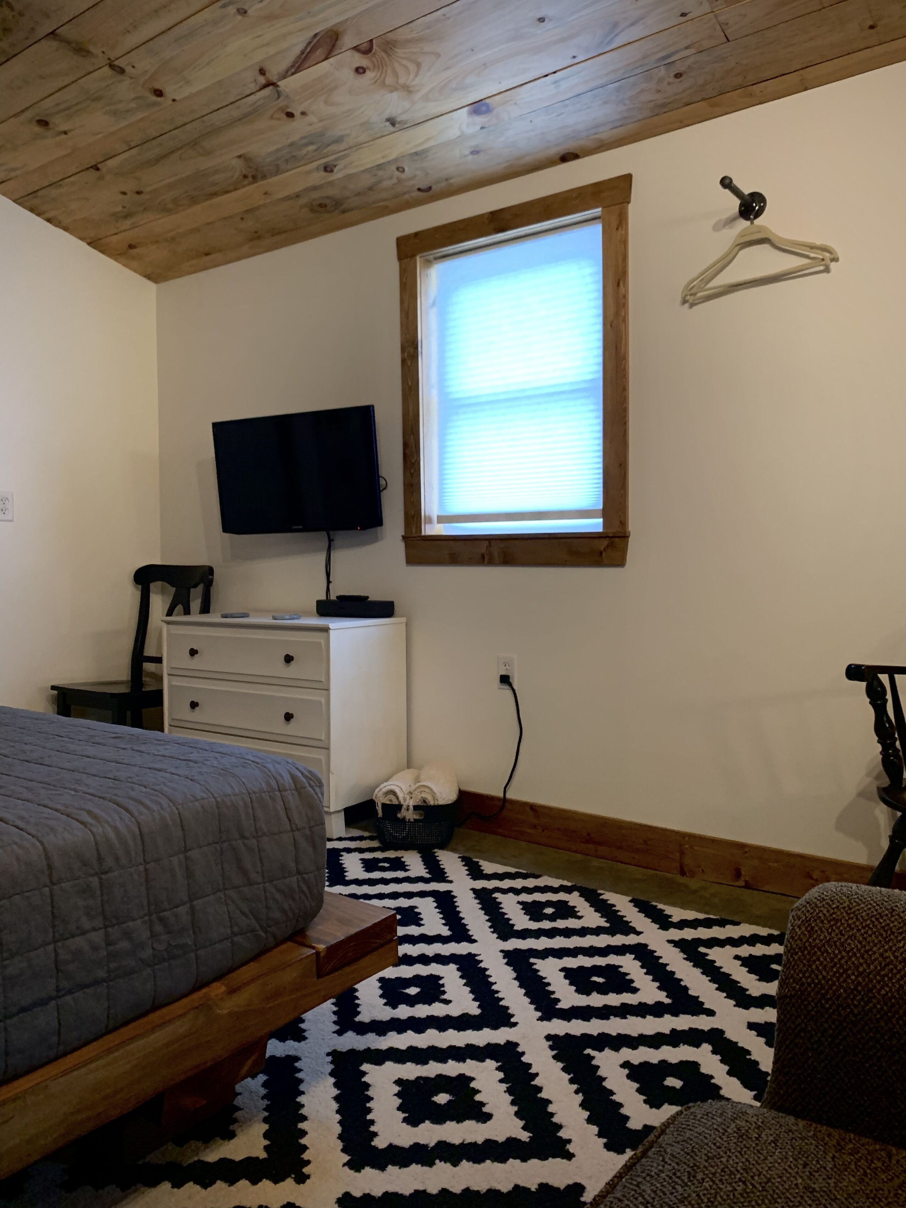 A bedroom with a bed, a dresser, a television, a window, and a patterned rug.