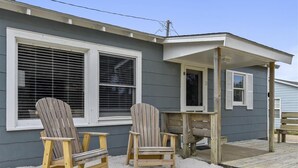 Uma casa com duas cadeiras Adirondack na área externa, varanda coberta e deck de madeira.