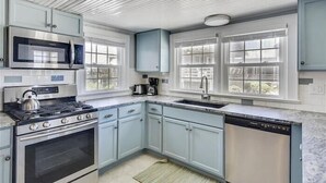 A modern kitchen with stainless steel appliances, light blue cabinets, and a large window providing natural light. - 6 bedroom, classic old nags head style oceanfront with a hot tub! (Nags Head)