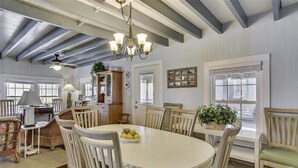 A dining area with a white oval table, wooden chairs, and a chandelier. - 6 bedroom, classic old nags head style oceanfront with a hot tub! (Nags Head)