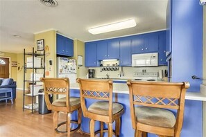 A kitchen with blue cabinets, a white refrigerator, and a coffee maker. There are three wooden chairs with cushioned seats. - 3 Bedroom with a private pool and hot tub in SNH! Short walk to the beach. (Nags Head)