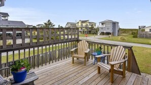 Una terraza de madera con dos sillas Adirondack y una mesita, con vistas a una zona residencial con casas y cielo despejado.