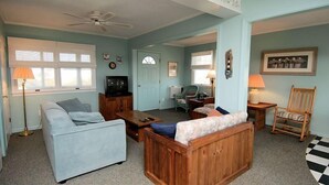Un salon avec un canapé, une chaise en bois, un téléviseur et une lampe.