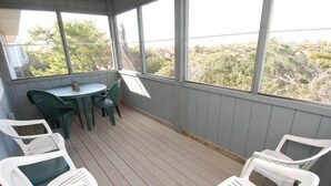 Un espace extérieur abrité doté d’une terrasse en bois, d’une table avec des chaises et de grandes fenêtres offrant une vue sur le paysage environnant.