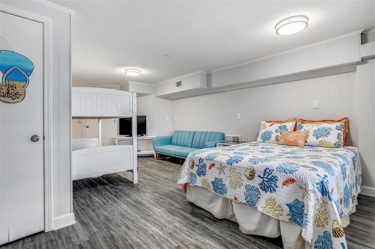 A bedroom with a bunk bed, a bed with a floral bedspread, a blue sofa, and a television.