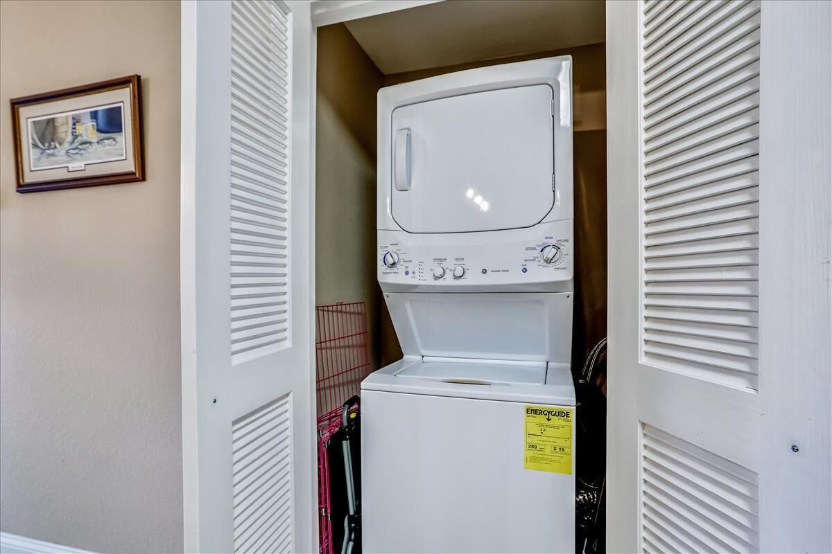 A laundry room with a stacked washer and dryer, a yellow energy guide sticker, and a framed picture on the wall.