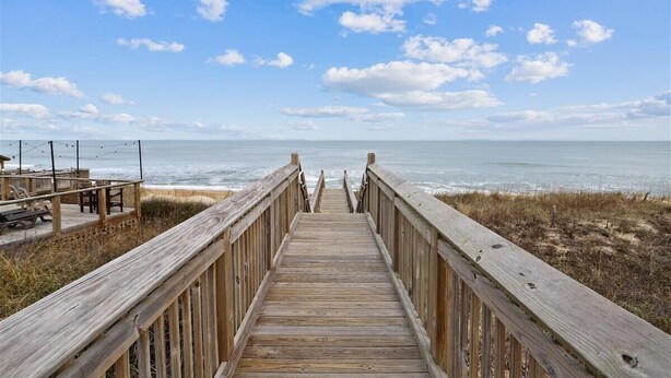 Ein Holzsteg führt zum Strand mit freiem Blick auf das Meer.