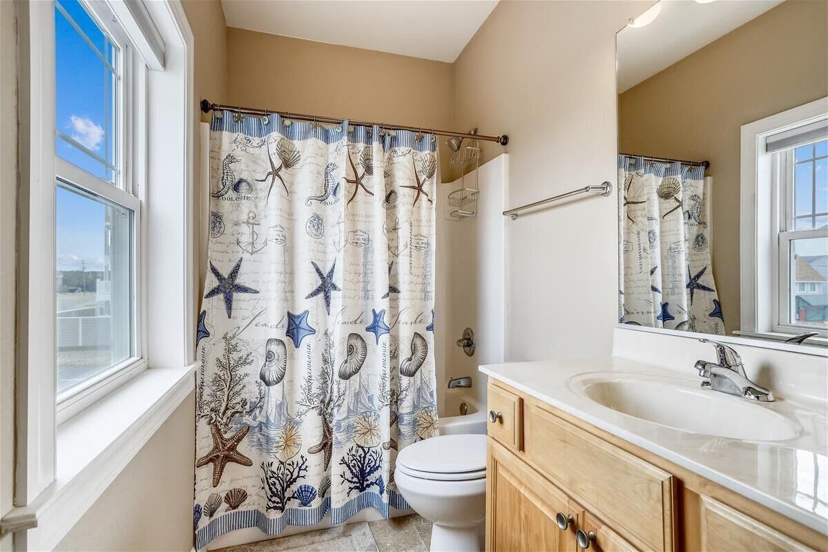 A bathroom with a nautical-themed shower curtain, a white sink, and a wooden vanity.
