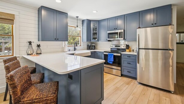 A modern kitchen with dark blue cabinets, stainless steel appliances, and a central island with wicker chairs. - Private pool and steps to the beach in quiet Southern Shores! Perfect beach home (Southern Shores)
