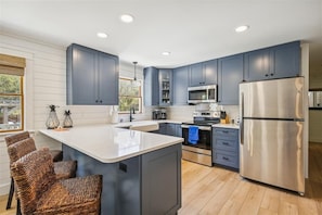 A modern kitchen with dark blue cabinets, stainless steel appliances, and a central island with wicker chairs.