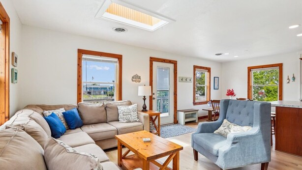 A spacious living room with a sofa, armchair, and coffee table, a dining area with a table and chairs, and large windows offering a view.