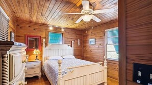 Un dormitorio de cabaña de madera con cama, cómoda, mesita de noche y ventilador de techo.