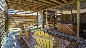 Eine Holzterrasse mit zwei Adirondack-Stühlen, einem Whirlpool und einem überdachten Bereich mit geneigtem Dach.