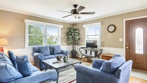 Un salon avec un ventilateur de plafond, deux canapés, une table basse, un téléviseur et une plante en pot.